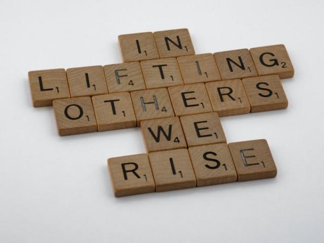 In scrabble letters, the message "In lifting others we rise"