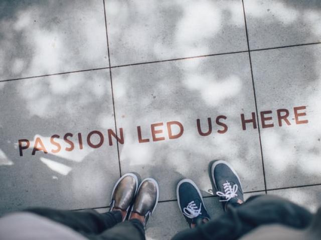 Looking down at a sidewalk, with two pairs of legs, the message "Passion led us here"